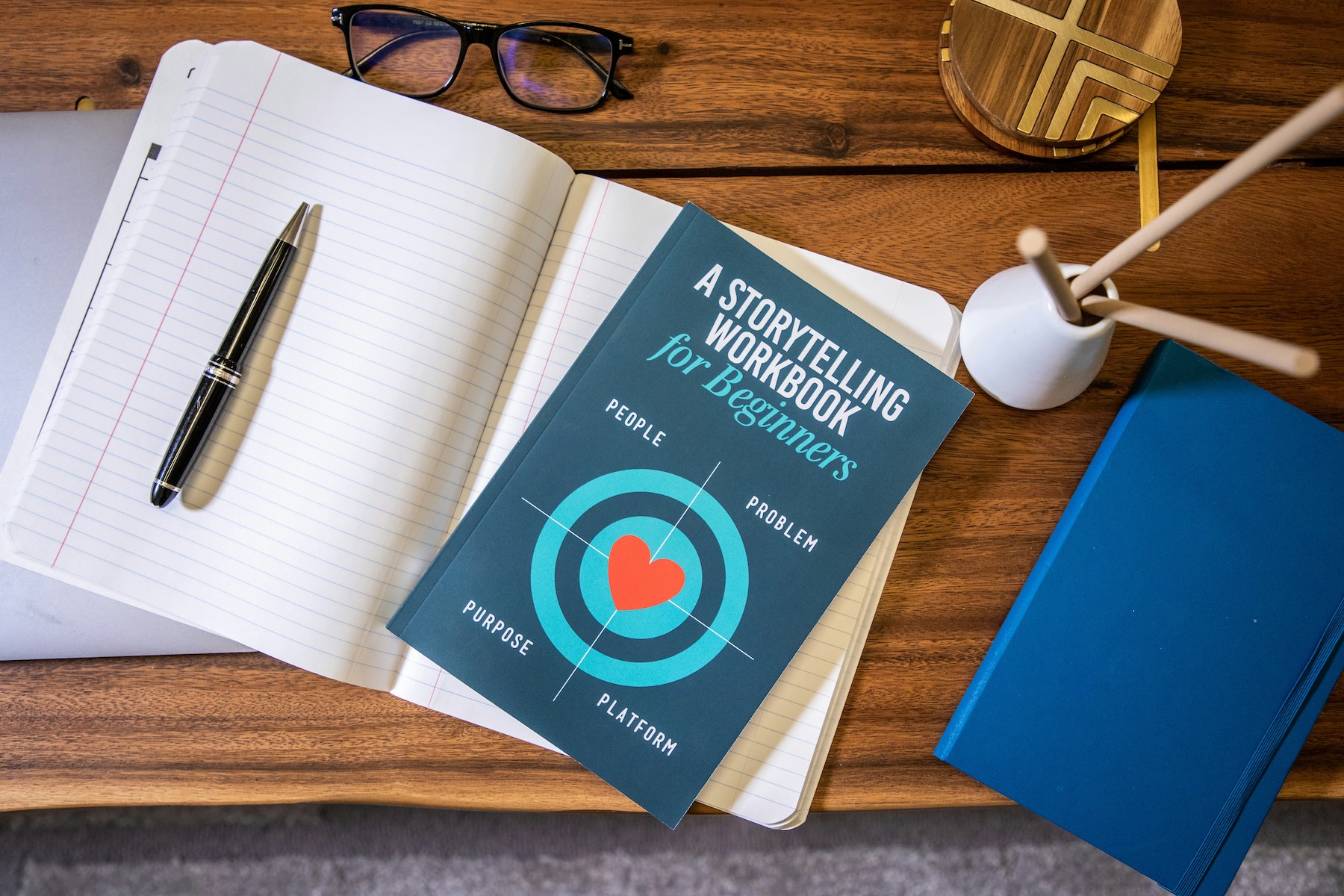 rain-bennett-Z5JJifMtbCo-unsplash A Storytelling Workbook for Beginners’ Book Stacked on Notebook on Desk